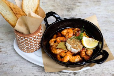 Gambas Al Pil Pil 'i sarımsaklı ekmekle birlikte gri arka plandaki aperatiflere izole edilmiş bir tabakta servis ediyor.