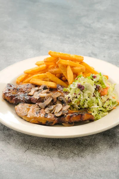 Specialty Grilled Pork Chop with salad and french fries served in a dish isolated on background side view of fastfood