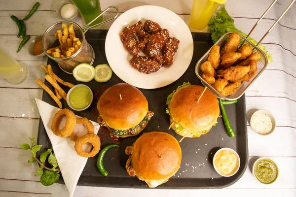 Brioche Chicken teriyaki Burger, Smash Double Beef Cheese Burger, Chicken Buffalo Wings, French Fries, wedges, lime, onion rings isolated on table assorted fastfood
