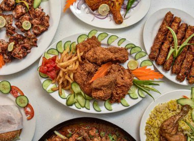 Kızarmış tavuk, biryani, tikka boti, kabas, hamburger, salata ve patates kızartması gri arka planda servis edilen Hint yemeği, Pakistanlı
