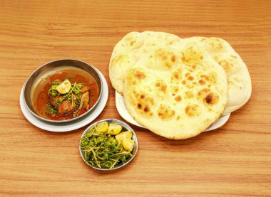 Baharatlı tavuk korma khamiri roti, limon dilimi ve salata ahşap masa başı Hint yemeği manzaralı bir tabakta servis edilir.