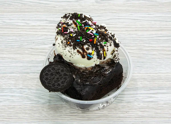 Oreo, brownie with Vanilla ice cream topping with vanilla chips, chocolate chips, sprinkles and bunties served in disposable cup side view of indian and pakistani dessert