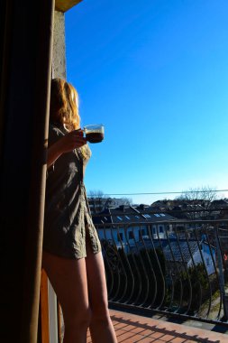 Güzel kız güneşin altında balkonda kahve içiyor.