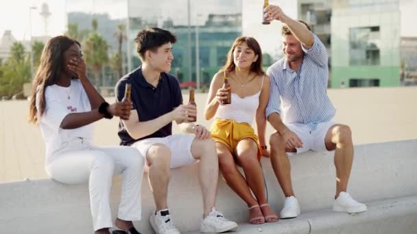 Jovens amigos inter-raciais felizes batendo garrafas de cerveja, comemorando a amizade no encontro ao ar livre — Vídeo de Stock