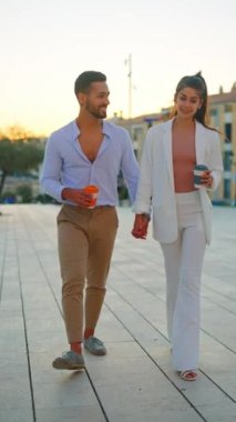 Son moda İspanyol çift sokakta dolaşırken paket kahve içiyor.