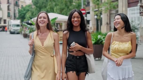 Três jovens mulheres felizes de etnias diferentes rindo de piada engraçada enquanto caminham no centro da cidade — Vídeo de Stock