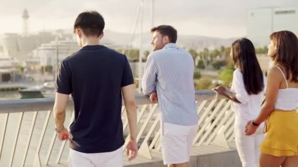 Multi-étnicos mejores amigos jóvenes de pie en el puente en el puerto deportivo al atardecer y charlando — Vídeo de stock
