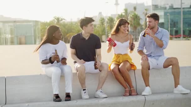 Cuatro personas multirraciales mejores amigos escuchando música y bebiendo cerveza en el terraplén al atardecer — Vídeos de Stock