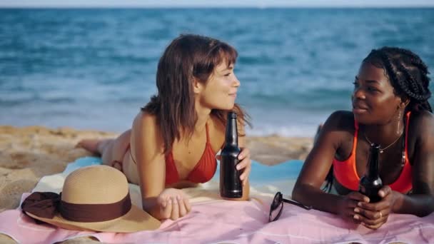 Студентки лежат на пляже и пьют пиво. — стоковое видео
