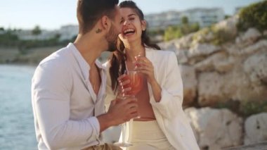 Kokteyllerle denize karşı öpüşen gülümseyen İspanyol çift.