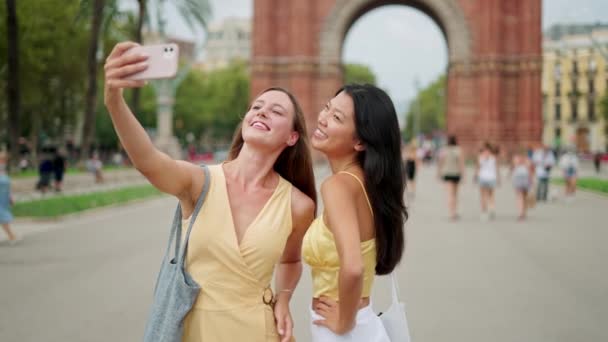 Duas jovens adoráveis e diversas amigas tirando fotos no celular ao ar livre perto do prédio histórico — Vídeo de Stock