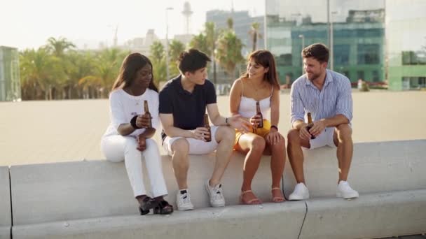 Τέσσερις νεαροί χαρούμενοι φίλοι διαφορετικών φυλών που μιλάνε και απολαμβάνουν αλκοολούχα ποτά στο ηλιοβασίλεμα — Αρχείο Βίντεο