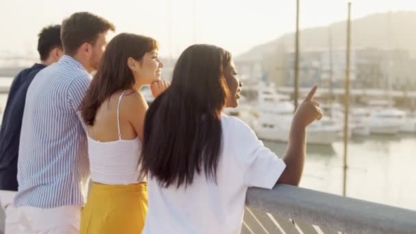 Mladé multiraciální přátelé těší úžasný západ slunce, zatímco stojí na mostě v přístavu a mluví — Stock video