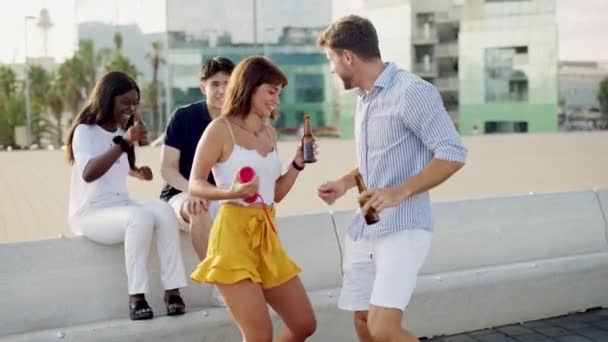 Молода щаслива пара танцює на музику бездротовим портативним динаміком, розслабляючись з друзями на вулиці — стокове відео