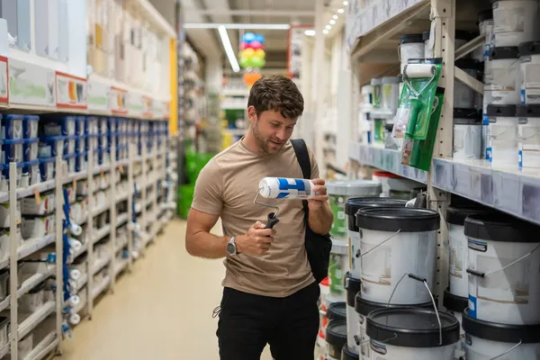 Hombre elegir rodillo de pintura en la tienda — Foto de Stock