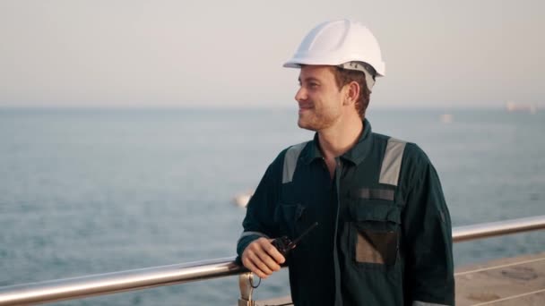 Happy dock worker with walkie-talkie in hand standing in port terminal, enjoying sea view — Stock Video