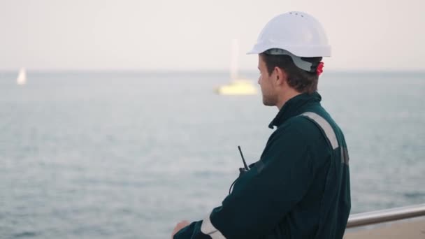 Νέος όμορφος άνθρωπος λιμενεργάτης με walkie-talkie στο χέρι έλεγχο της διαδικασίας εργασίας στο λιμάνι της ναυτιλίας — Αρχείο Βίντεο