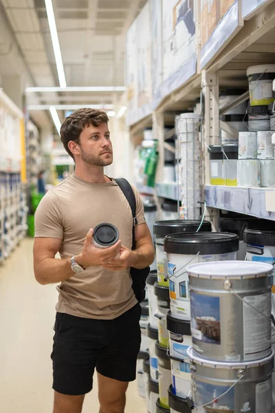 Hombre examinando latas de pintura en el estante — Foto de Stock