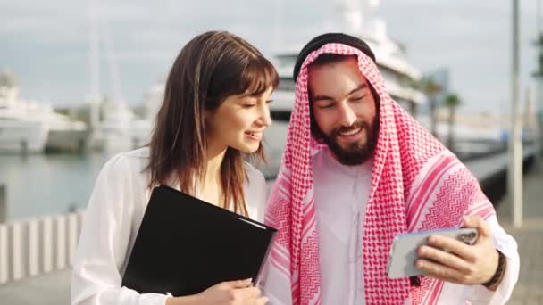 Homme d'affaires arabe souriant montrant quelque chose sur smartphone à son assistante européenne attrayante — Video
