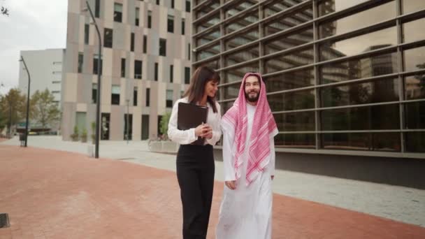 Arabisk affärsman och europeisk affärskvinna talar glatt och leende när du går city street — Stockvideo