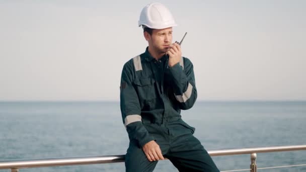 Jovem trabalhador portuário em capacete e macacão usando rádio vhf, controlando o processo de trabalho no porto de navegação — Vídeo de Stock