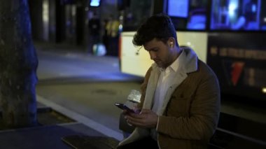 Geceleri bankta akıllı telefon kullanan bir erkek.