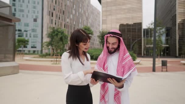 Улыбающаяся женщина показывает арабскому бизнесмену место для подписания контракта на встрече на открытом воздухе — стоковое видео