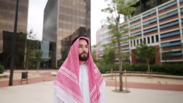 Confident handsome arab man in traditional saudi clothes standing alone at empty square outdoors — Stock Video