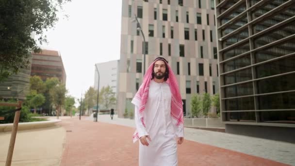Exitoso sheikh árabe hombre en ropa tradicional mirando rascacielos mientras camina calle de la ciudad — Vídeos de Stock