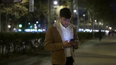 Karanlık sokakta cep telefonuna bakan bir adam