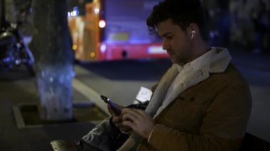 Geceleri bankta akıllı telefon kullanan bir erkek.