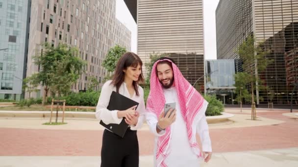 Dua rekan yang beragam berbicara dengan tim online melalui smartphone selama perjalanan bisnis di Dubai — Stok Video