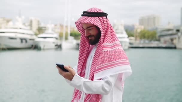 Pengusaha arab berpakaian tradisional dengan smartphone di pelabuhan, membaca berita internet di telepon genggam — Stok Video