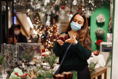 Beyaz maskeli mutlu genç kadın kış tatili alışveriş turunun tadını çıkarıyor.