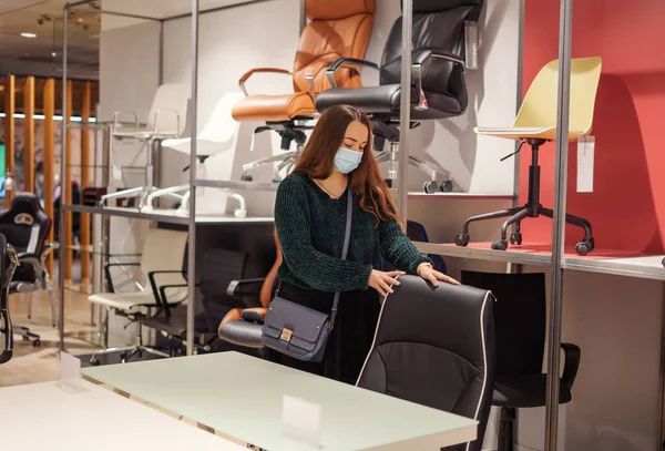 Young woman in white face protective mask choosing office furniture during covid-19 pandemic Royalty Free Stock Images