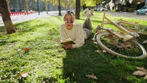 Frau liest Buch auf Gras neben Holzfahrrad — Stockvideo