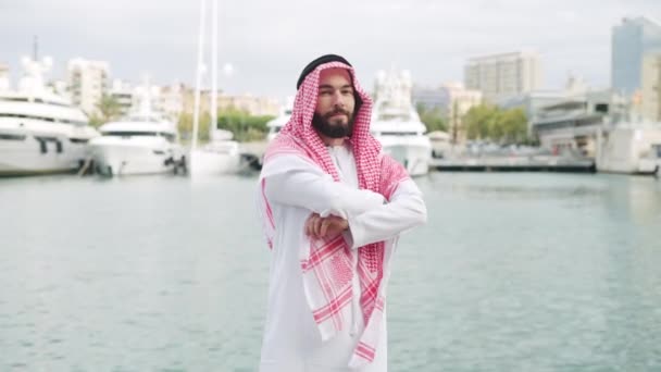 Selamat tersenyum saudi pria berpose di luar ruangan dalam pakaian tradisional dengan lengan disilangkan di pelabuhan — Stok Video