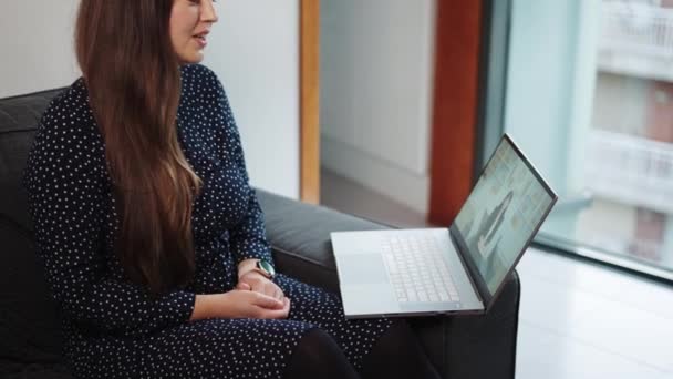 Mujer joven sentada en el sofá en casa conversando con el terapeuta virtual en el portátil — Vídeo de stock