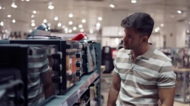 Dükkanda mikrodalga fırın seçen adam.
