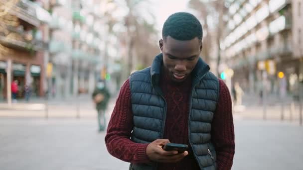 Чорний чоловік переглядає смартфон і ходить у місті — стокове відео