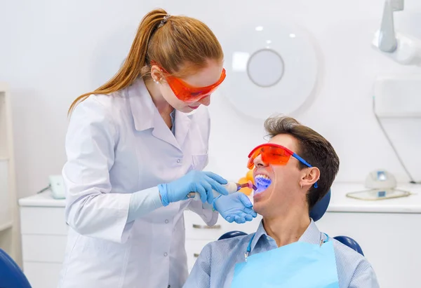 Зубной врач со светом лечит зубы пациента — стоковое фото