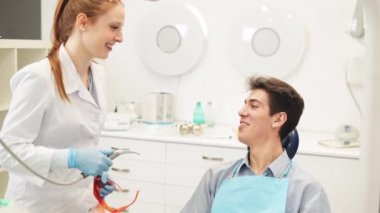 Pozitif dişçi ve erkek hasta tedavi öncesi diş kliniğinde eğleniyor ve gülüyorlar.