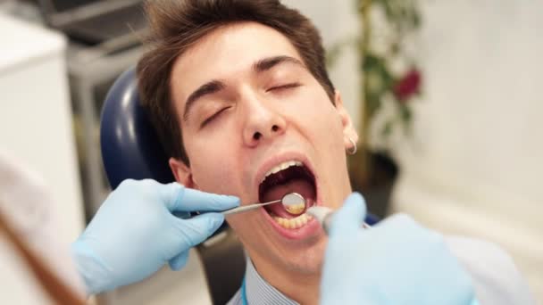 Стоматолог, использующий стоматологические инструменты для проверки чувствительности зубов пациента мужского пола — стоковое видео