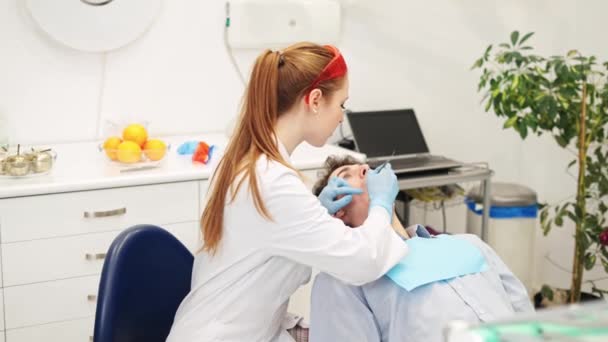 Dentista femenina que trata el diente de un paciente varón joven acostado en una silla dental, llenando el conducto radicular — Vídeo de stock