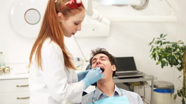 Genç bayan dişçi, muayene sırasında ağız aynası olan erkek hastayı muayene ediyor. — Stok video