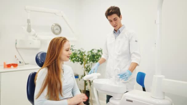 Молодая пациентка в стоматологическом кресле промывает рот водой перед посещением стоматолога — стоковое видео