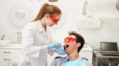 Dişi dişçi, dişlerini doldurduktan sonra gülümseyen erkek hastayla konuşuyor.