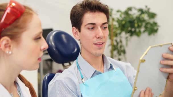 Молодой человек разговаривает с женщиной-дантистом перед процедурой отбеливания зубов — стоковое видео