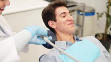 Klinikte diş tedavisi sırasında ağzı durulanan gülümseyen genç erkek hasta.