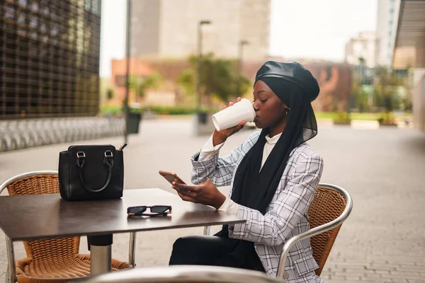 Negro elegante mujer beber café y navegar por teléfono inteligente —  Fotos de Stock